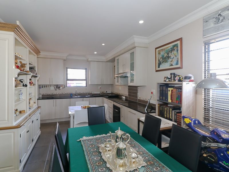 Open-plan kitchen and dining area featuring modern cabinetry, dark granite countertops, integrated appliances, and recessed ceiling lighting.