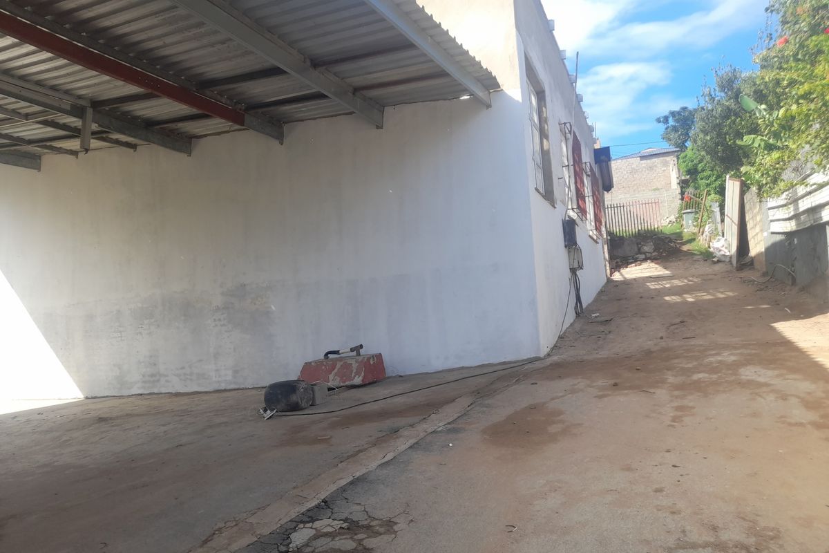 Rear exterior view of the industrial property featuring a covered concrete parking or loading area with a metal roof structure and adjacent dirt access path.