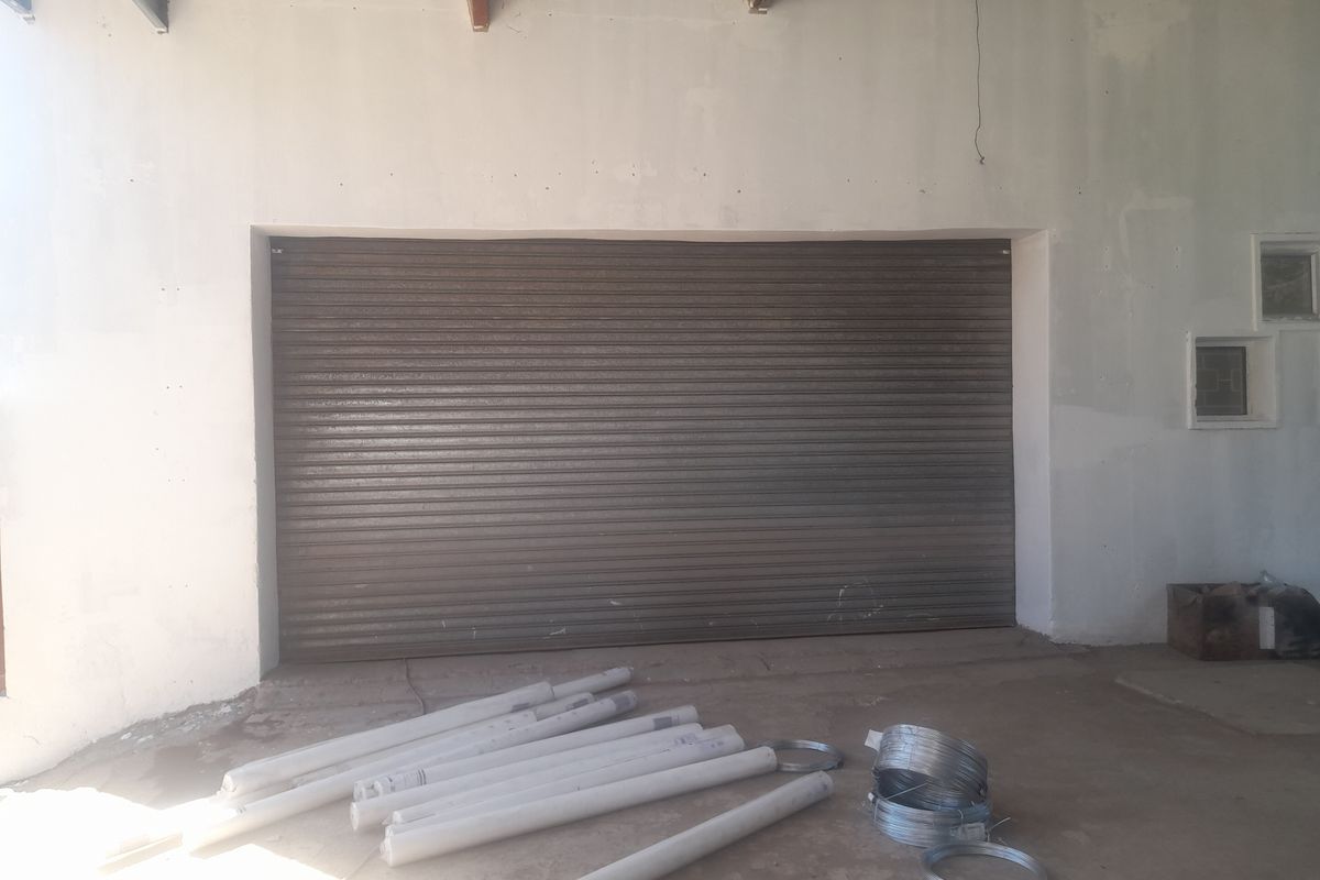 Industrial garage space featuring a large roller shutter door, concrete flooring, and exposed steel roof beams, suitable for storage or workshop use.