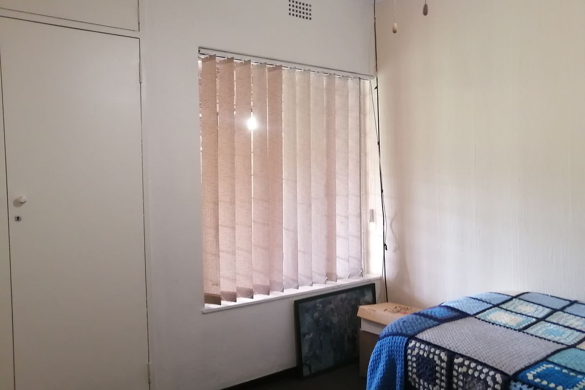 A functional bedroom featuring built-in cupboards and vertical window blinds, offering a simple and practical living space.