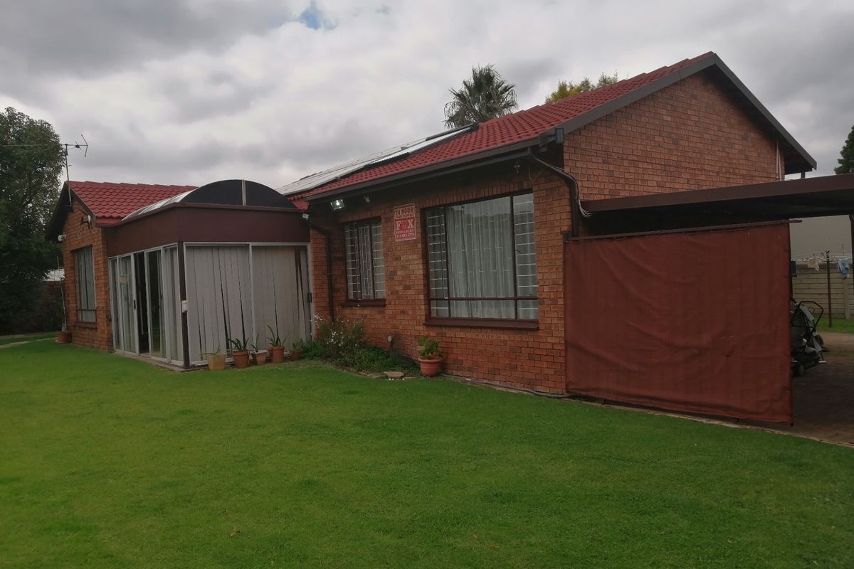 Rear view of a single-story brick house featuring a sunroom extension, tiled roof, security bars on windows, and a covered carport area.