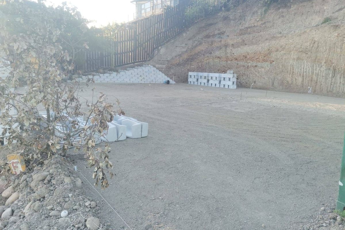 A vacant residential plot featuring a graded area, retaining wall structures, and a timber boundary fence, ready for development.