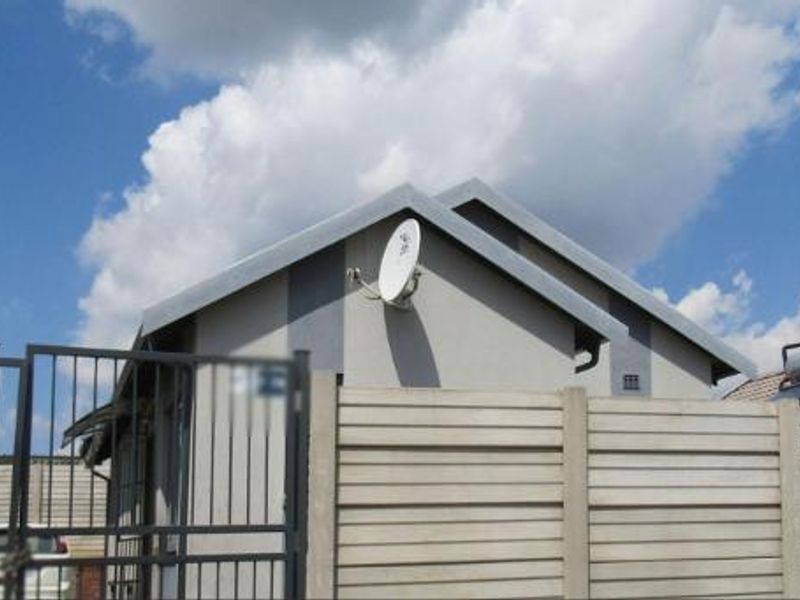 Front view of the property featuring a precast concrete boundary wall, metal security gate, and roof-mounted solar water heating system.