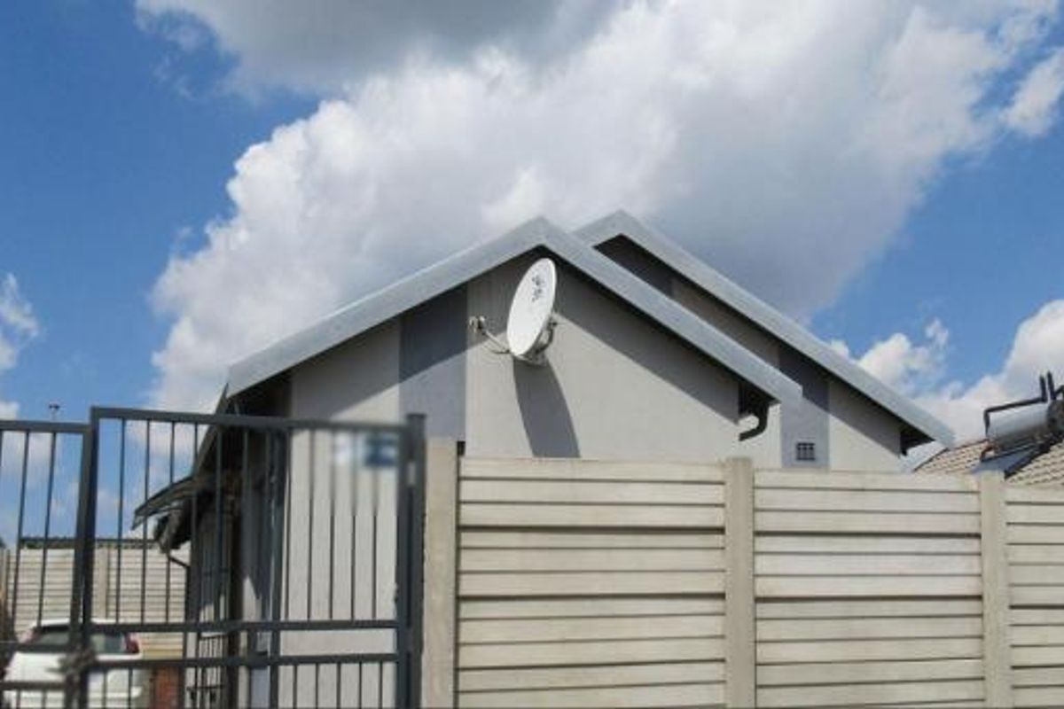 Front view of the property featuring a precast concrete boundary wall, metal security gate, and roof-mounted solar water heating system.