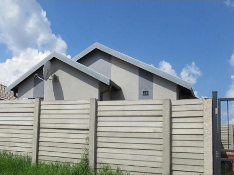 Front view of a residential property featuring a secure precast concrete boundary wall, metal gate, and a pitched roof structure.