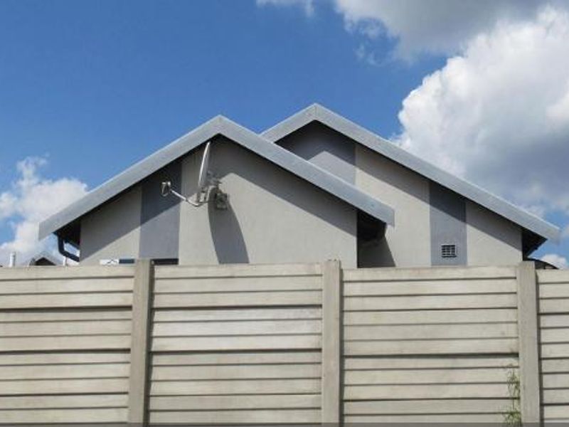 A view of the property's front exterior, featuring a precast concrete boundary wall, metal gate, and a pitched roof structure.