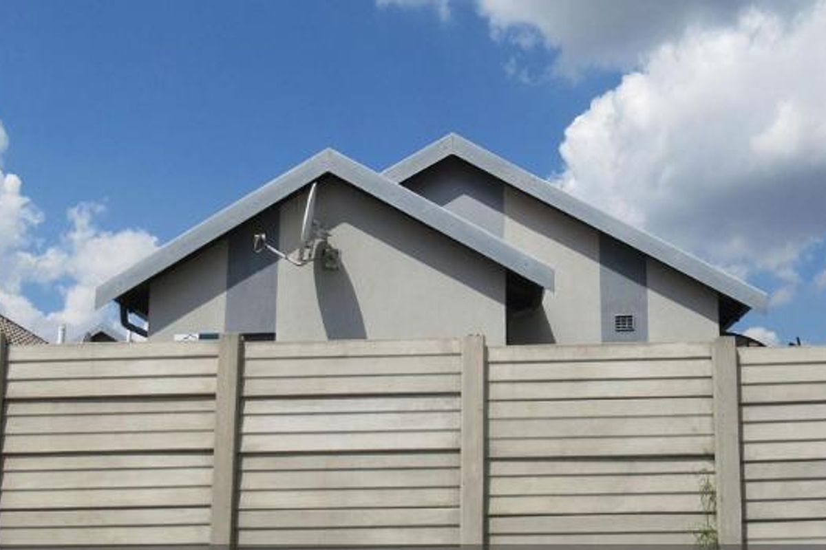 A view of the property's front exterior, featuring a precast concrete boundary wall, metal gate, and a pitched roof structure.