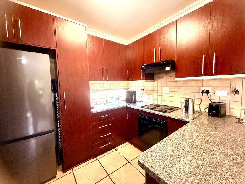 A functional kitchen featuring dark wood-finish cabinetry, granite countertops, tiled backsplash, and built-in cooking appliances including an oven and hob.