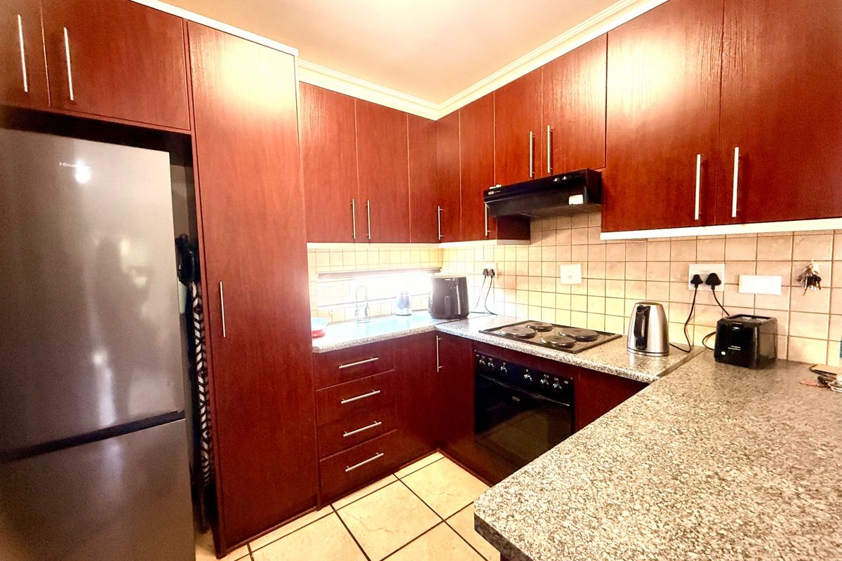 A functional kitchen featuring dark wood-finish cabinetry, granite countertops, tiled backsplash, and built-in cooking appliances including an oven and hob.