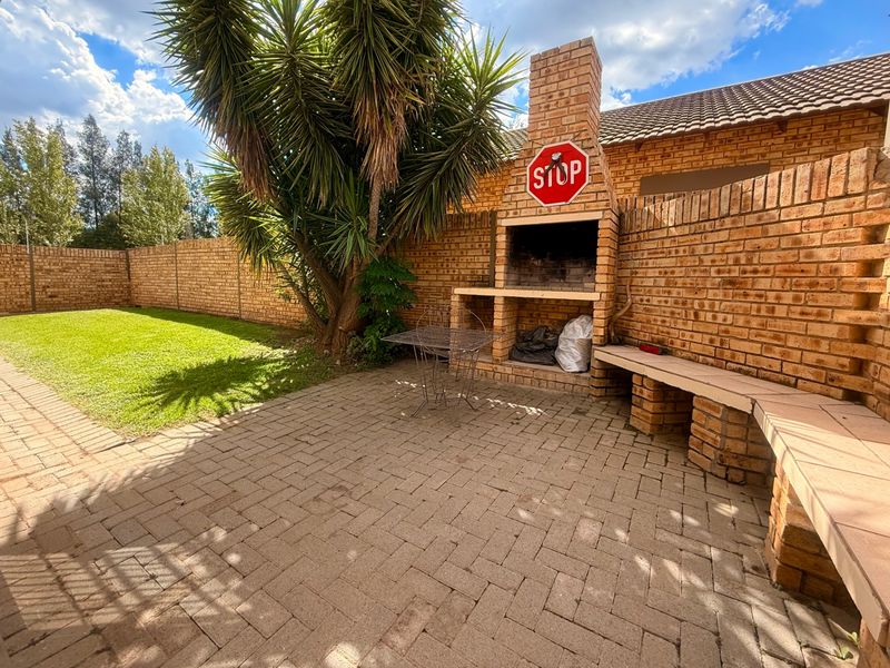 Outdoor patio area featuring a built-in brick braai, integrated brick bench seating, and paved flooring, overlooking a private garden space.