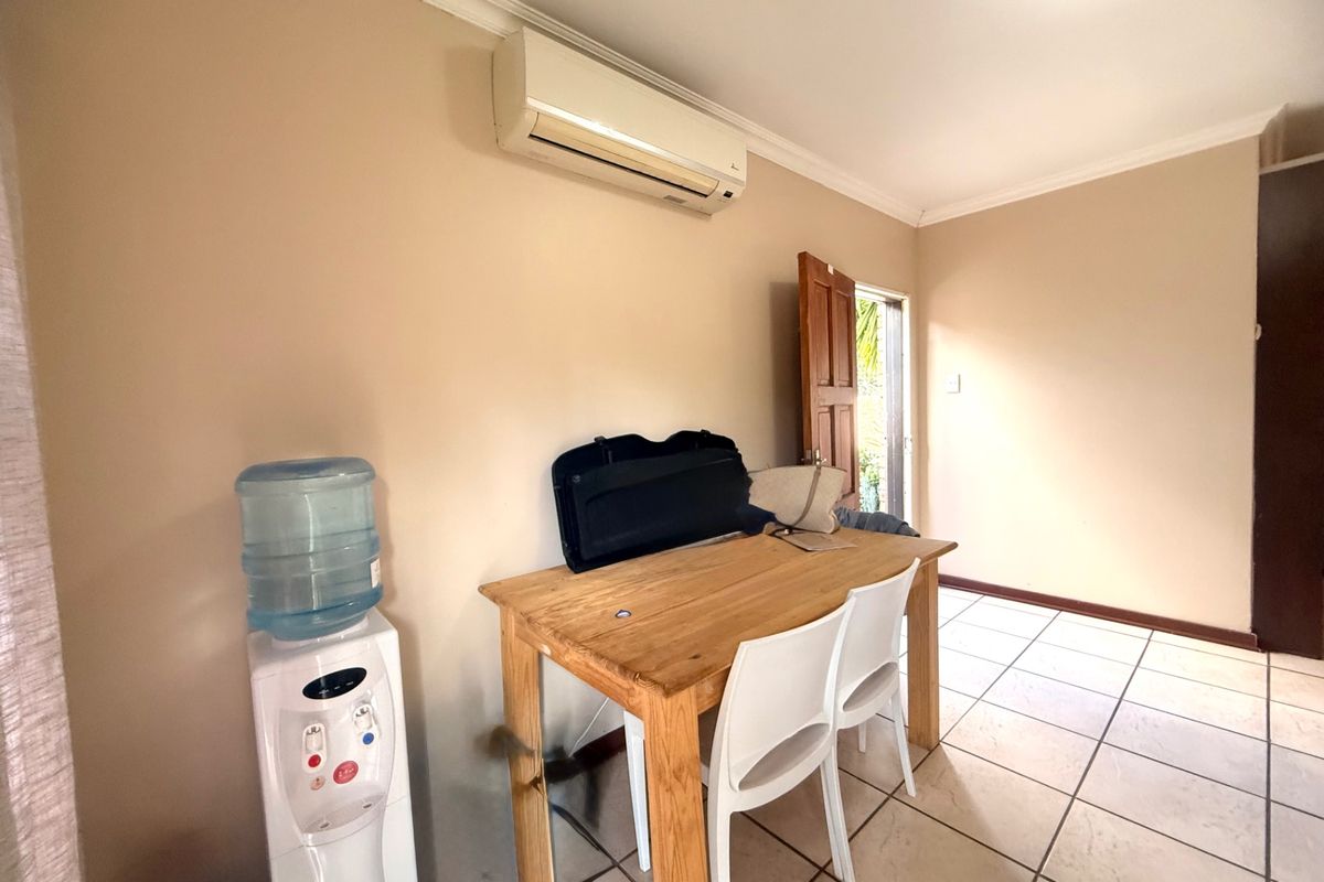 A functional living area featuring tiled flooring, coving, and a wall-mounted split-system air conditioner, with direct access to an outdoor space.