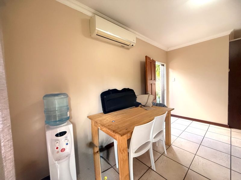 A functional living area featuring tiled flooring, coving, and a wall-mounted split-system air conditioner, with direct access to an outdoor space.