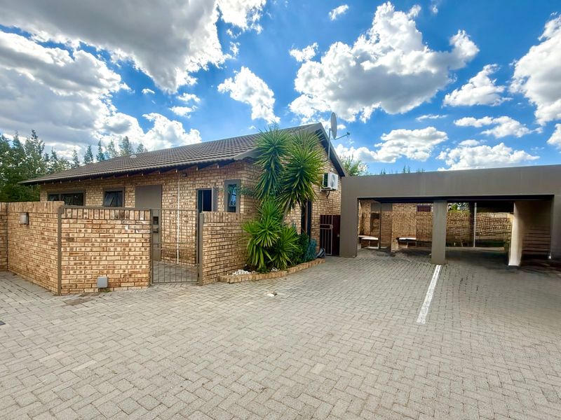 Front exterior view of a facebrick townhouse featuring a paved driveway, covered carport, and secure boundary walling.