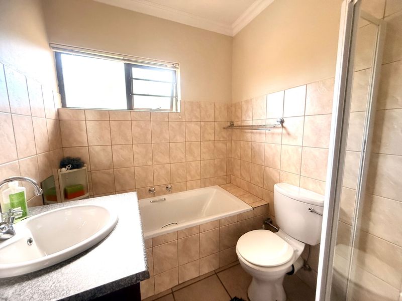 A functional bathroom featuring a built-in bathtub, vanity basin, toilet, and a separate shower enclosure with neutral wall tiling.