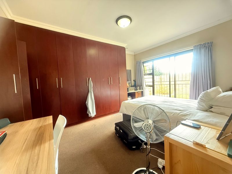 A spacious bedroom featuring extensive built-in wooden cupboards, carpeted flooring, and a sliding door providing access to the exterior.