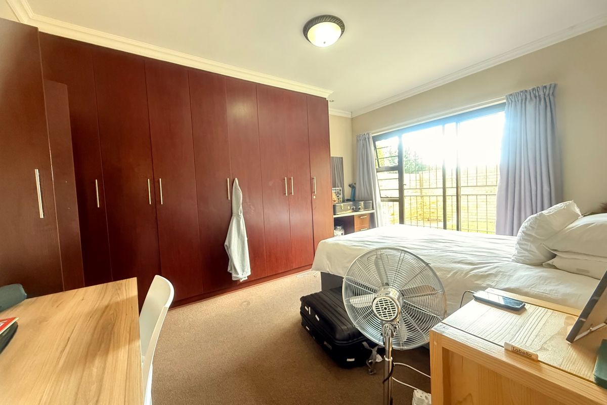 A spacious bedroom featuring extensive built-in wooden cupboards, carpeted flooring, and a sliding door providing access to the exterior.