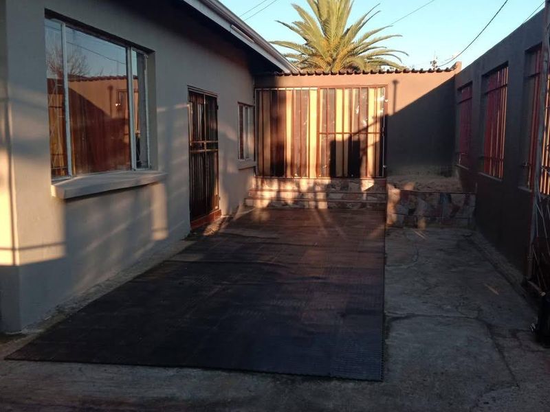 A rear exterior courtyard area featuring concrete paving, a raised planter bed, and secure metal-framed windows and doors.