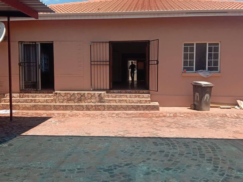 Rear view of a single-story house featuring a tiled roof, paved patio area, and security gates at the main entrance points.