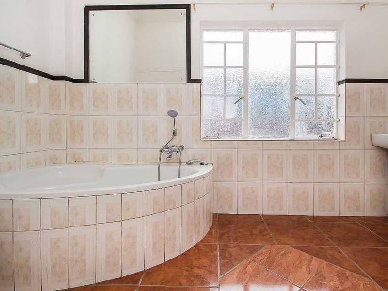 A dated bathroom featuring a corner bathtub, pedestal basin, and tiled finishes, offering a blank canvas for a modern renovation.