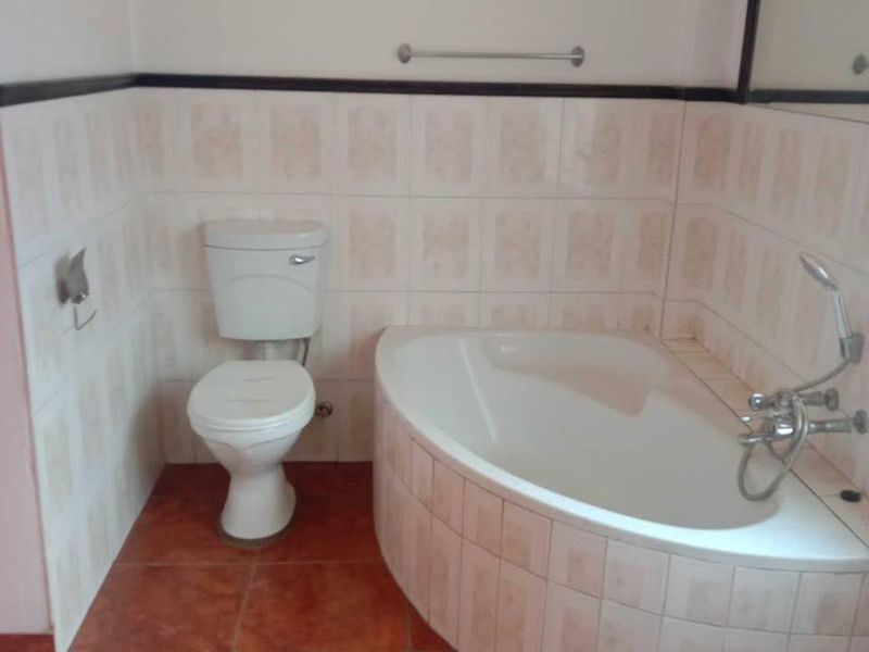 A dated bathroom featuring a built-in corner bathtub, toilet, and tiled finishes throughout.