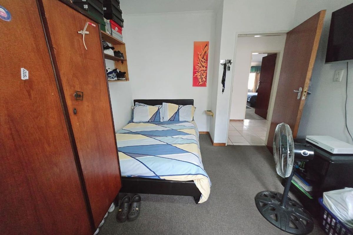 A compact bedroom featuring neutral walls, carpeted flooring, and built-in shelving, providing a functional space with direct access to the hallway.
