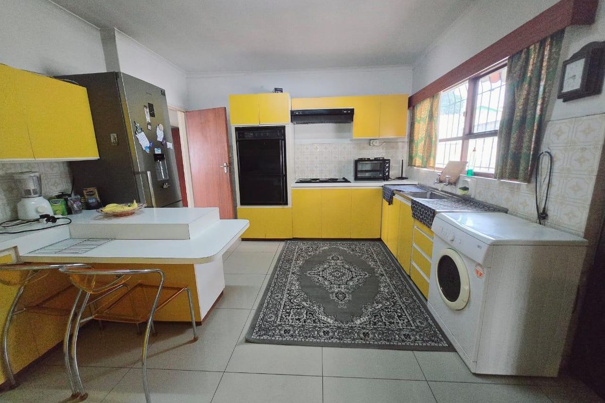 A functional kitchen featuring bright yellow cabinetry, built-in oven, extractor fan, and tiled flooring with a practical layout for daily meal preparation.
