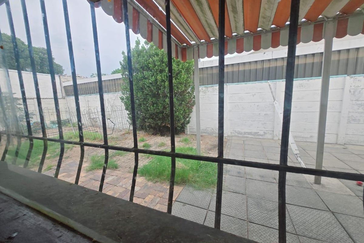 Rear exterior view featuring a paved patio area, retractable awning, and precast concrete boundary wall, viewed through a window with security bars.