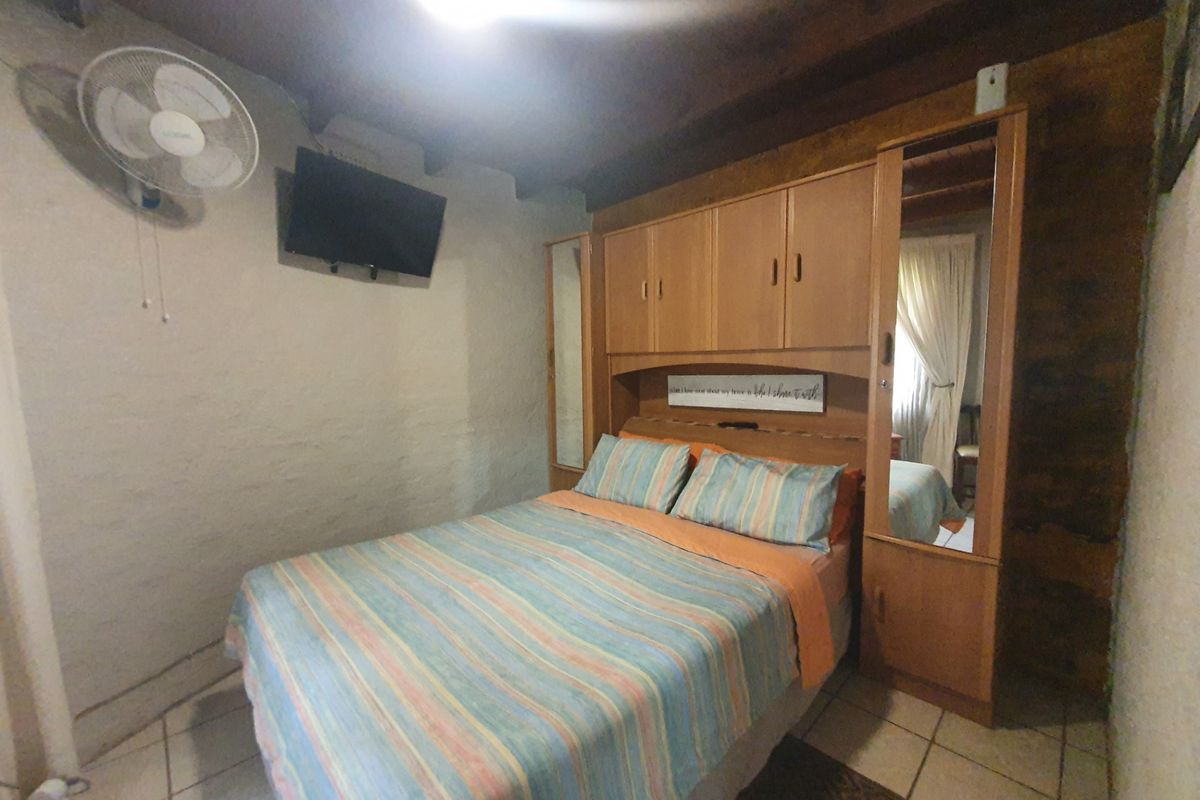 A bedroom featuring built-in cabinetry, tiled flooring, and an exposed timber ceiling, providing a functional sleeping space.