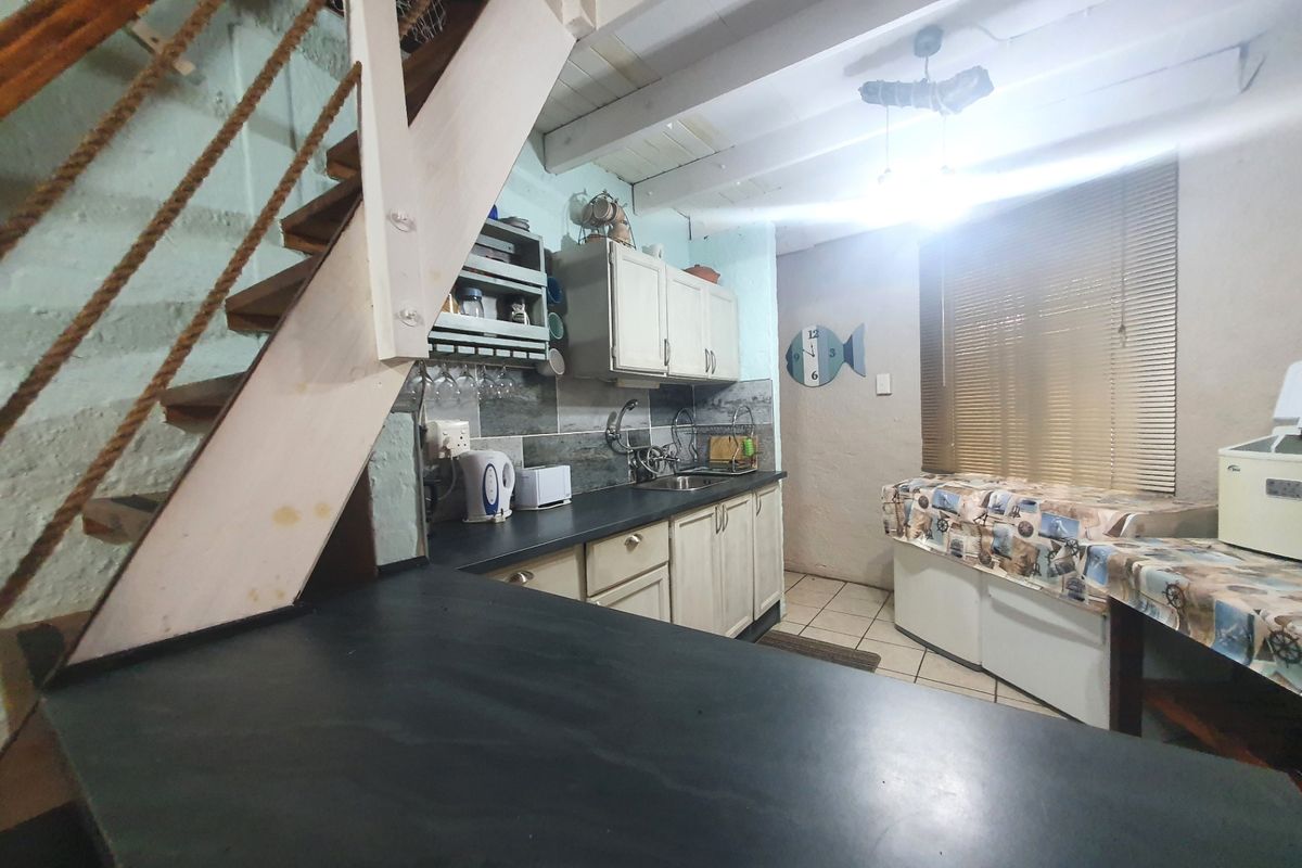 A compact kitchen featuring built-in cabinetry, a stainless steel sink, and exposed timber ceiling beams, with an adjacent timber staircase leading to an upper level.