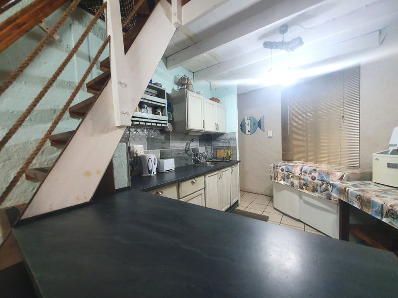 A compact kitchen featuring built-in cabinetry, a stainless steel sink, and exposed timber ceiling beams, with an adjacent timber staircase leading to an upper level.