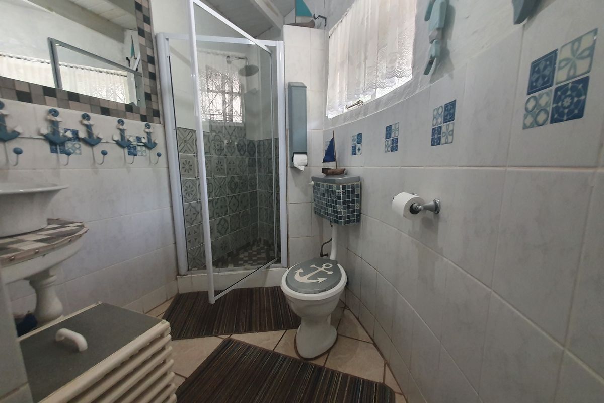 A functional bathroom featuring a shower enclosure, pedestal basin, and toilet with tiled finishes throughout.