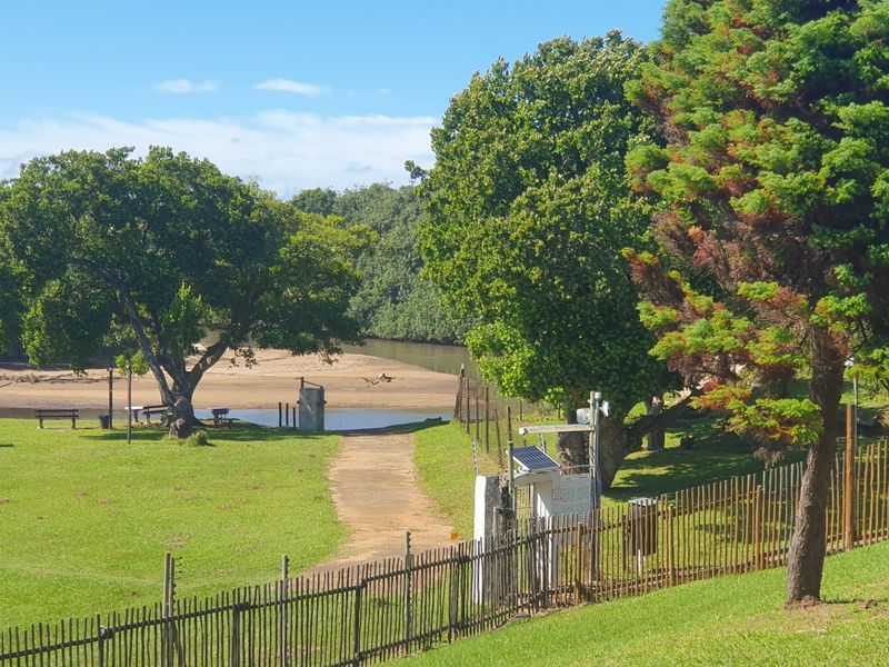A well-maintained garden area featuring a paved pathway, electric fencing, and security infrastructure, leading towards a natural riverbank setting.