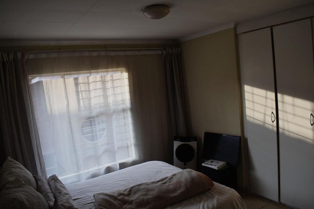 A bedroom featuring built-in cupboards and a window with security bars, providing natural light.