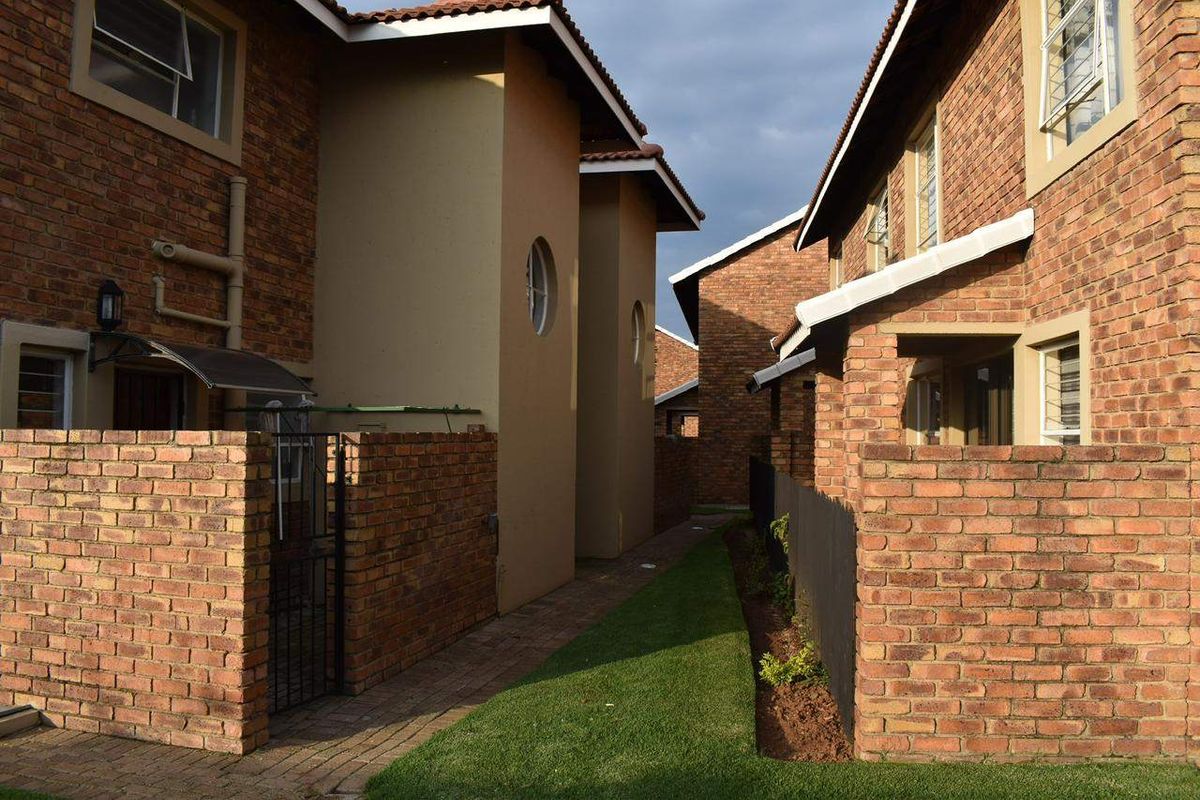 Exterior view of townhouse units featuring face-brick facades, paved walkways, and small private garden sections between the buildings.