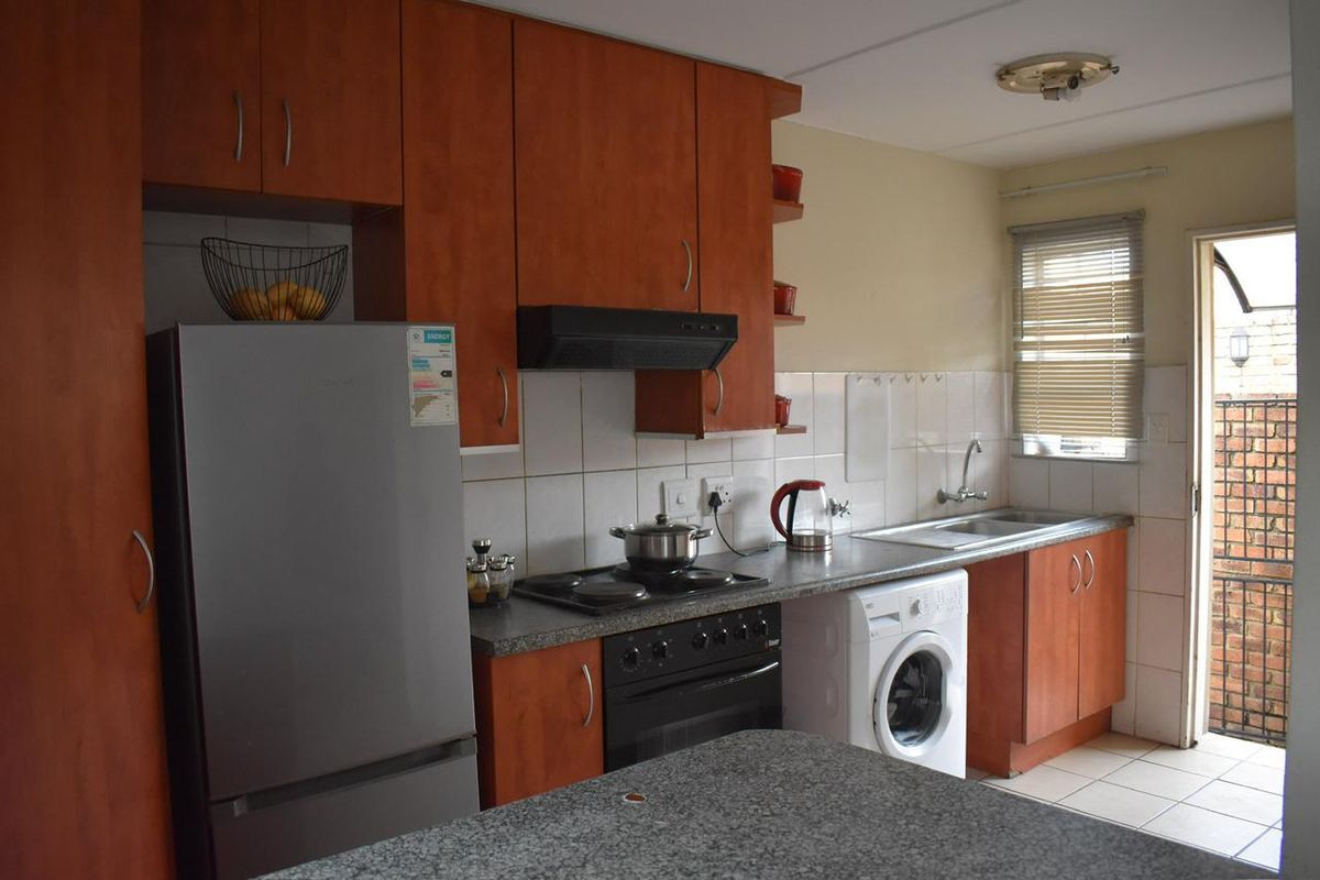 Functional kitchen featuring wood-look cabinetry, granite-style countertops, built-in oven with hob, extractor fan, and dedicated space for laundry appliances.