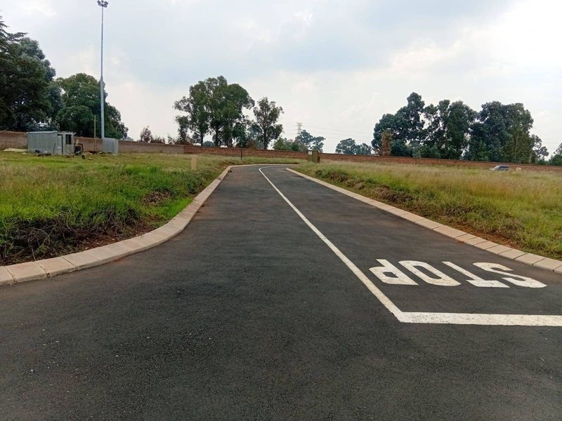 A paved access road with clear road markings, concrete kerbing, and surrounding perimeter walling in a residential estate setting.