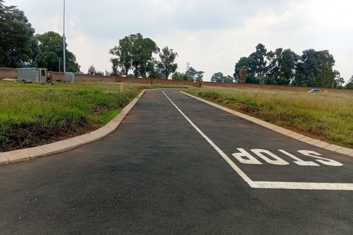 A paved access road with clear road markings, concrete kerbing, and surrounding perimeter walling in a residential estate setting.