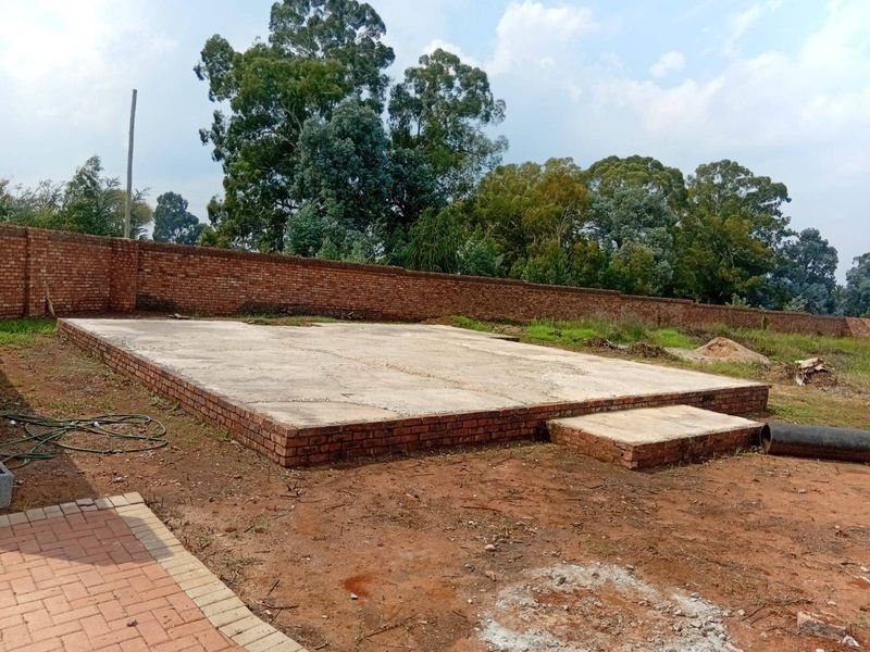 An outdoor area featuring a concrete slab foundation and brick boundary wall, currently in an unfinished state.