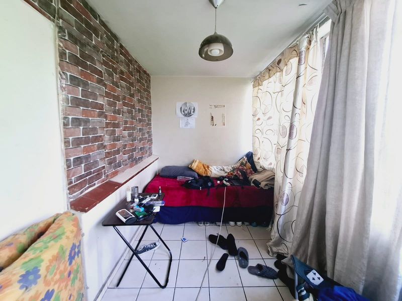 A compact bedroom featuring a brick veneer accent wall and ceramic tiled flooring, offering a functional space with potential for modernization.