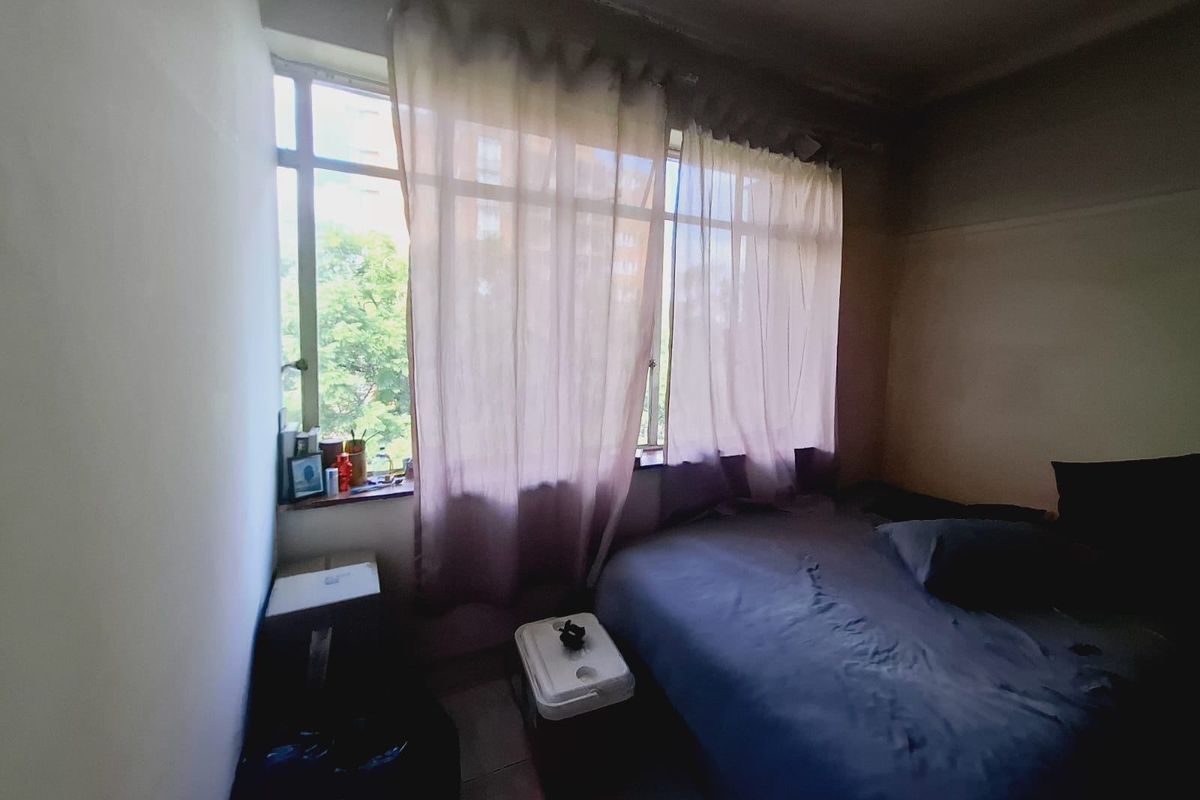 A bedroom featuring a large window providing natural light and tiled flooring, currently showing signs of wear and requiring cosmetic updates.