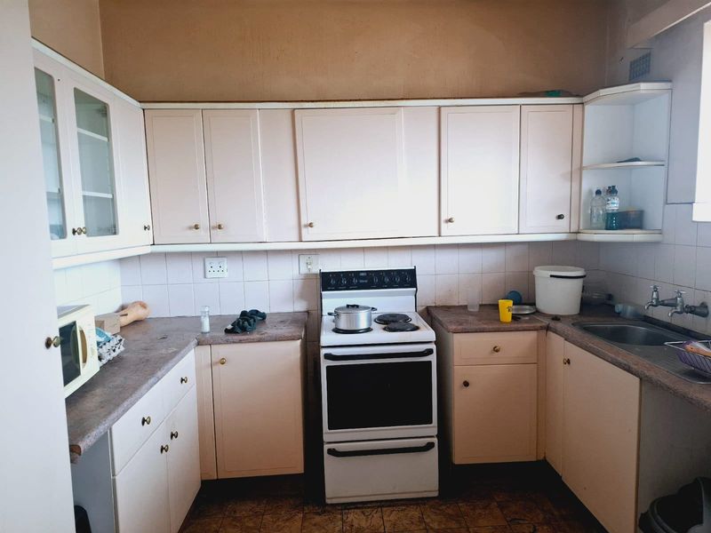 A dated kitchen featuring original cabinetry, laminate countertops, a freestanding stove, and a stainless steel sink, offering significant potential for modernization and renovation.