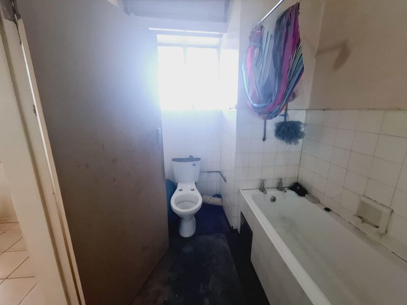 A dated bathroom featuring a standard bathtub and toilet, requiring renovation and cosmetic updates to improve its overall condition and appeal.