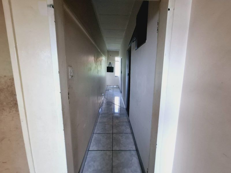 A narrow, empty hallway featuring tiled flooring and plain walls, showing signs of wear and surface staining throughout.