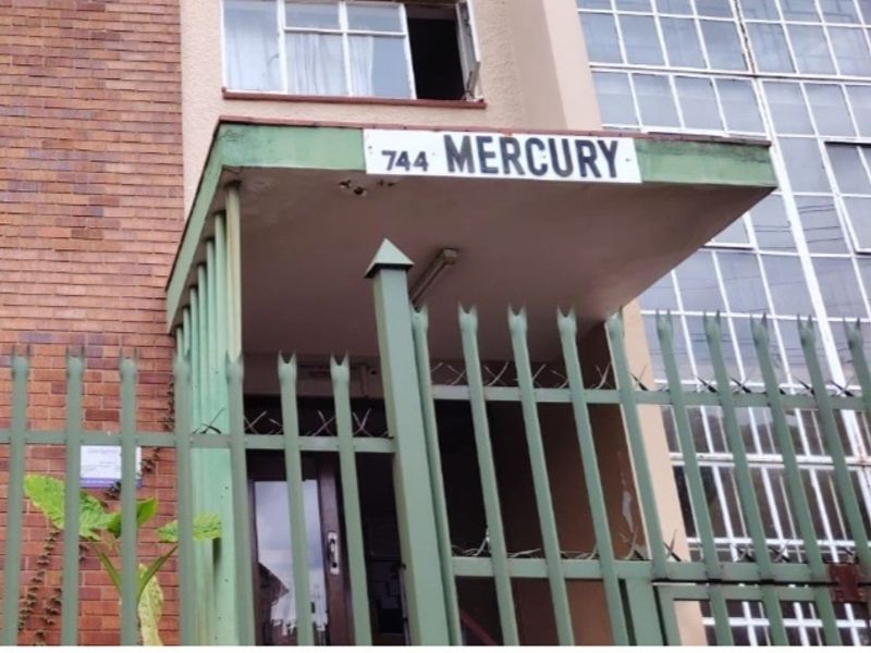 Front entrance view of the apartment building featuring a brick facade, metal security fencing, and a concrete entrance canopy.