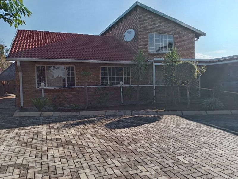 Front view of a face brick house featuring a tiled roof, grid windows, and a spacious paved driveway.