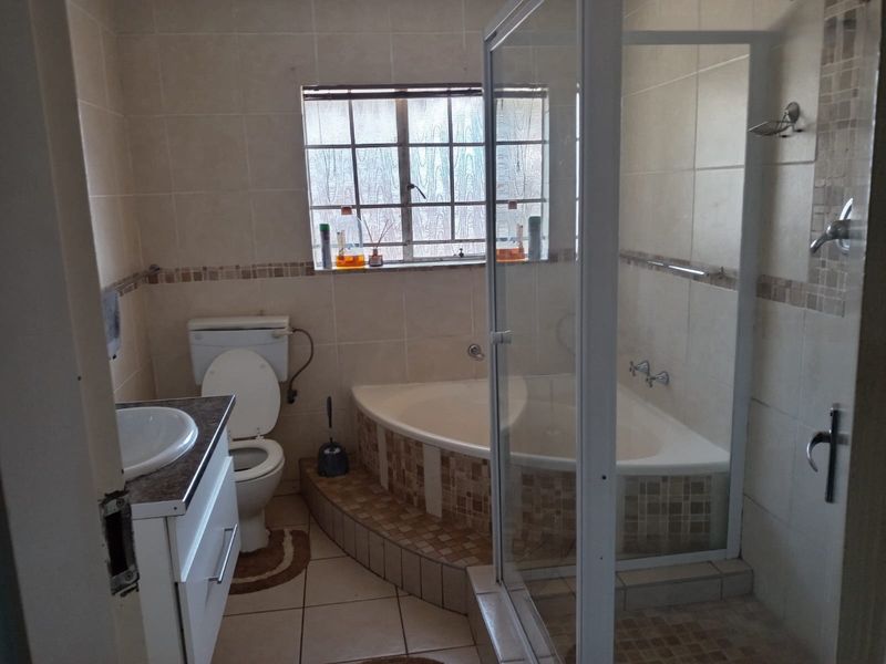 A functional bathroom featuring a corner bathtub, separate shower enclosure, built-in vanity with basin, and tiled finishes throughout.