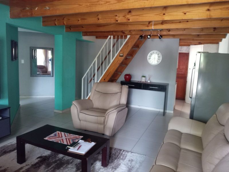 Open plan living area featuring exposed timber ceiling beams, tiled flooring, and a staircase with a metal railing.
