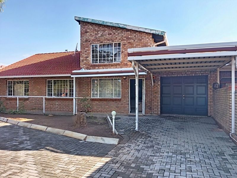 Front elevation of a brick house featuring a tiled roof, attached carport, and paved driveway area.