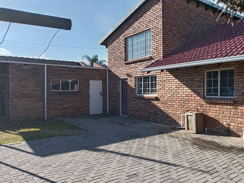 A rear exterior view of a double-story face brick house featuring a paved courtyard area and secure access points.