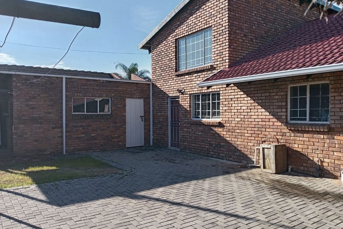 A rear exterior view of a double-story face brick house featuring a paved courtyard area and secure access points.